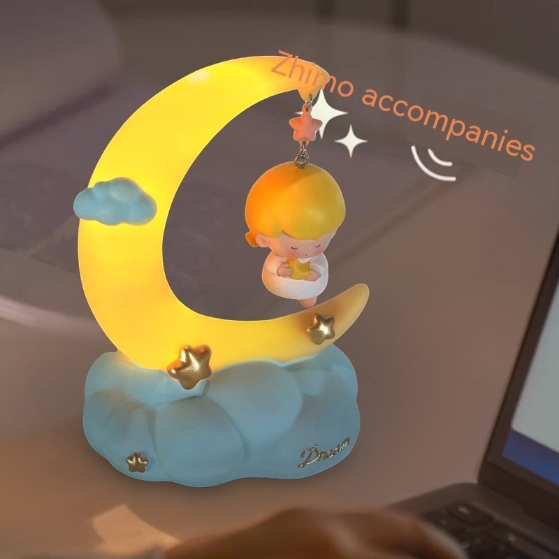 LX EMPIRE Little Angel night light with a glowing yellow moon, blue clouds, and stars. Made of resin and plastic.