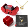 LX EMPIRE red apple-shaped jewelry box with preserved rose and gold necklace featuring a knot pendant with crystal.